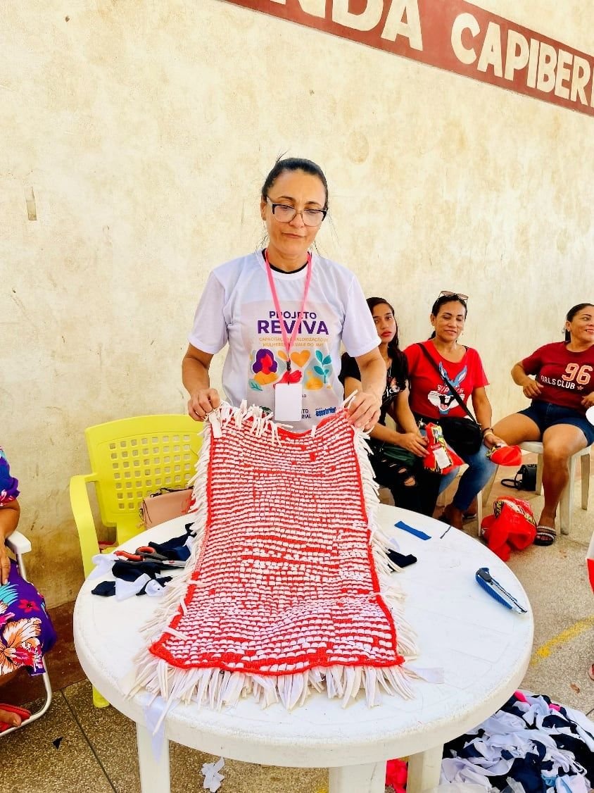 Mulher mostrando uma peça vermelha de crochê sobre uma mesa