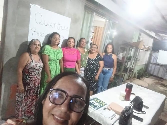 Mulheres reunidas em frente a uma casa, uma delas fazendo selfie em primeiro plano
