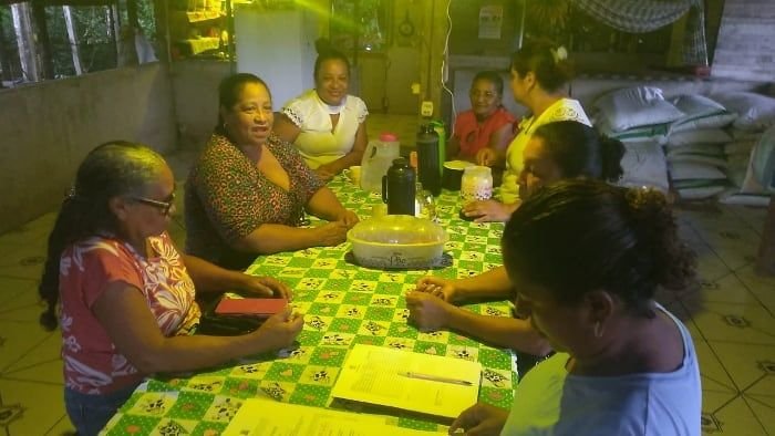 Mulheres conversando ao redor de uma mesa com toalha estampada, à noite