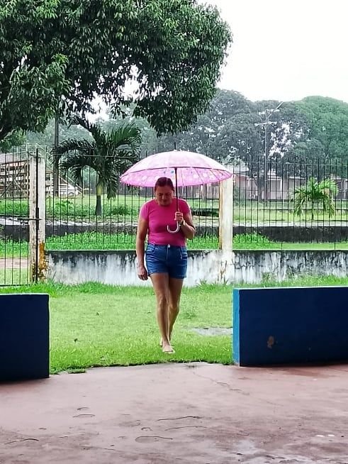 Mulher com guarda-chuva cor-de-rosa atravessando um gramado