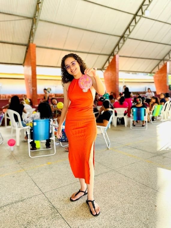 Mulher de vestido laranja sorrindo num pavilhão cheio de participantes