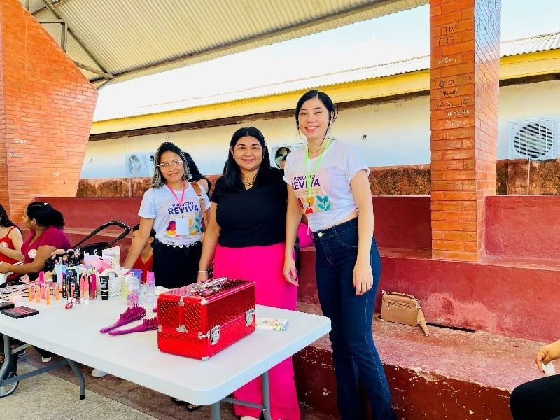 Três mulheres ao lado de uma mesa com maleta de maquiagem