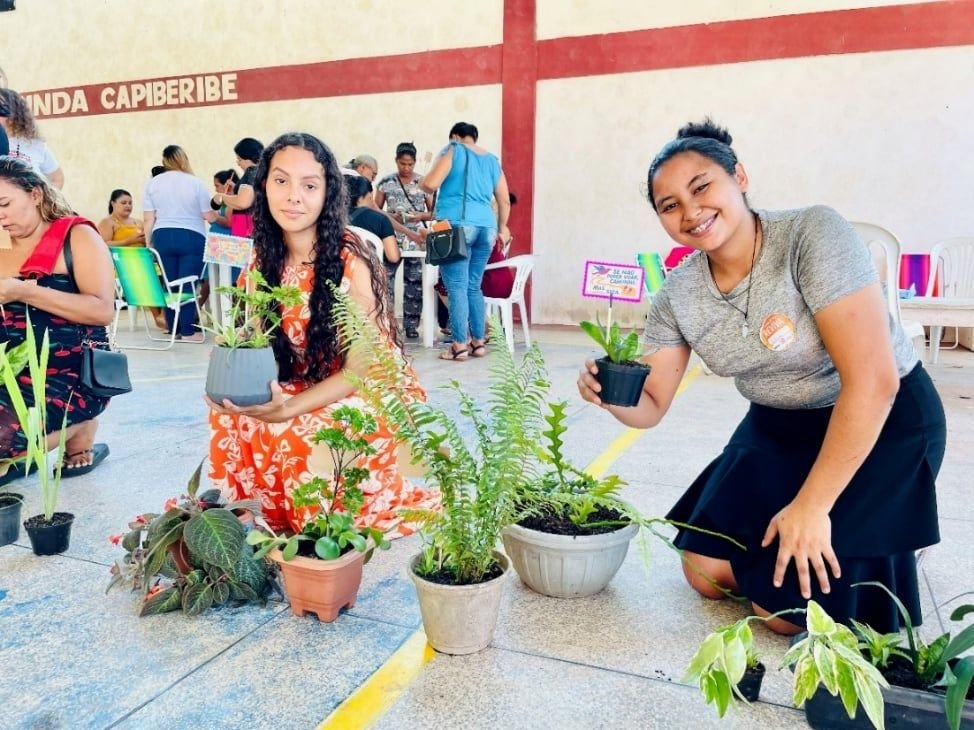 Duas jovens mostrando mudas de plantas em vasos