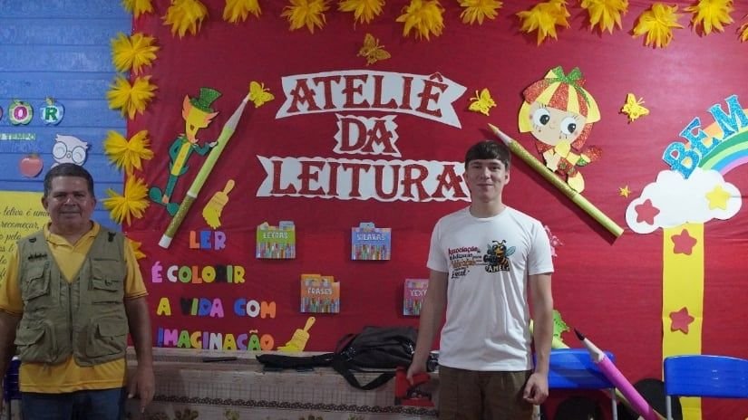 Duas pessoas em frente a um painel colorido do Ateliê da Leitura
