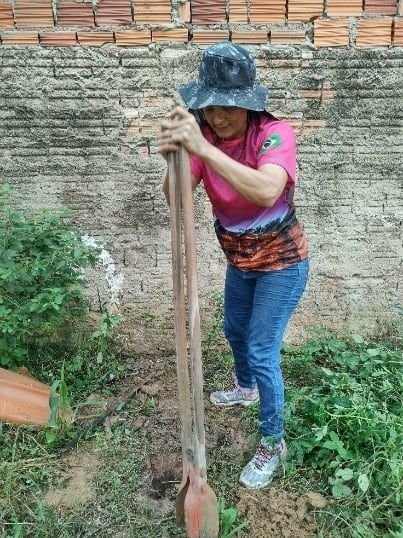 Mulher de chapéu trabalhando a terra com uma ferramenta