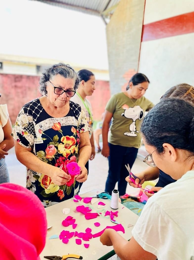 Mulheres montando flores de papel cor-de-rosa sobre uma mesa